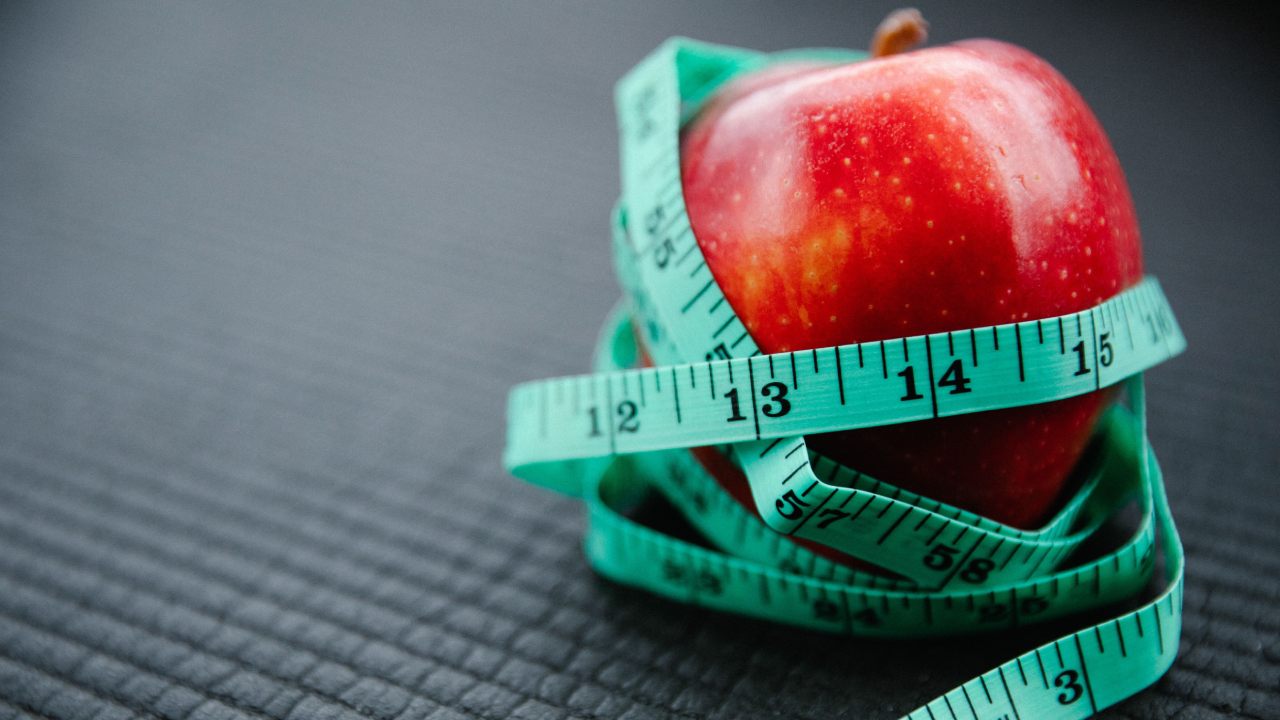 Mela rossa avvolta da un metro da sarta, simbolo di alimentazione equilibrata, nutrizione e benessere della pelle.